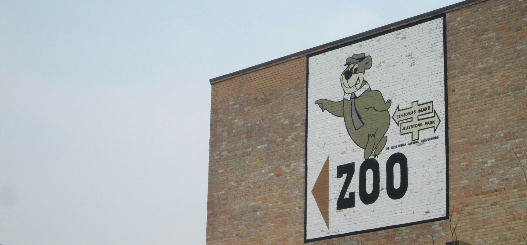 A vintage painted sign on a brick wall pointing the way to the zoo