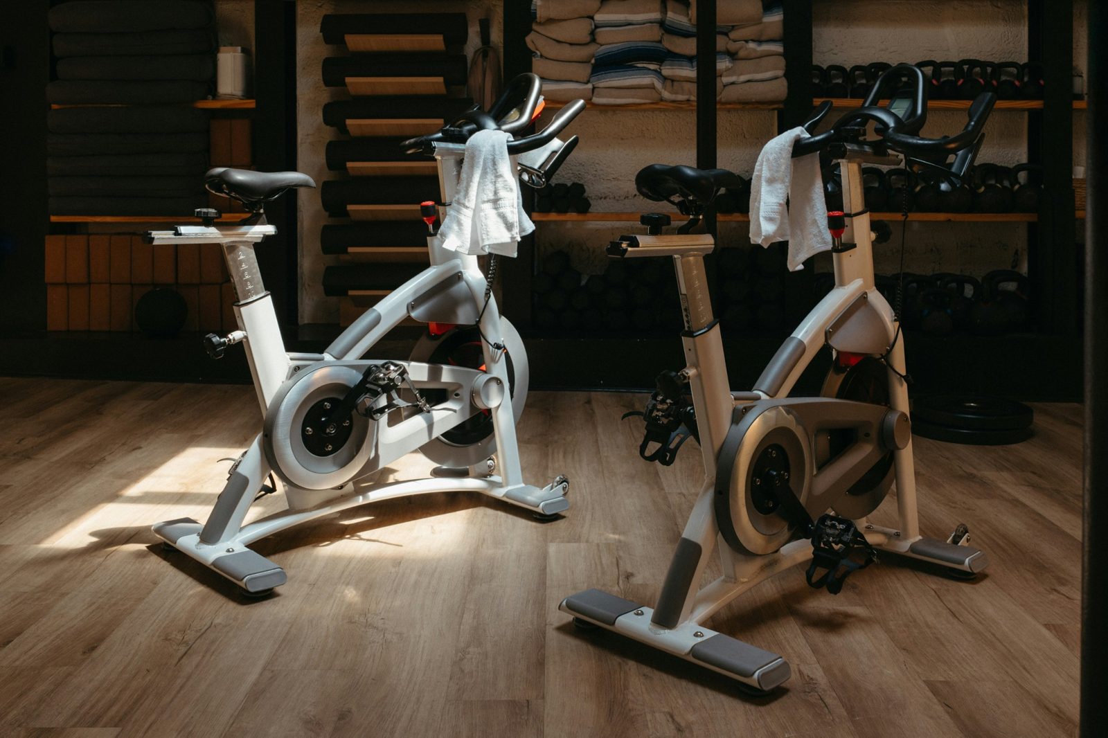 Two white spin bikes with towels draped over the handlebars in a sunlit studio