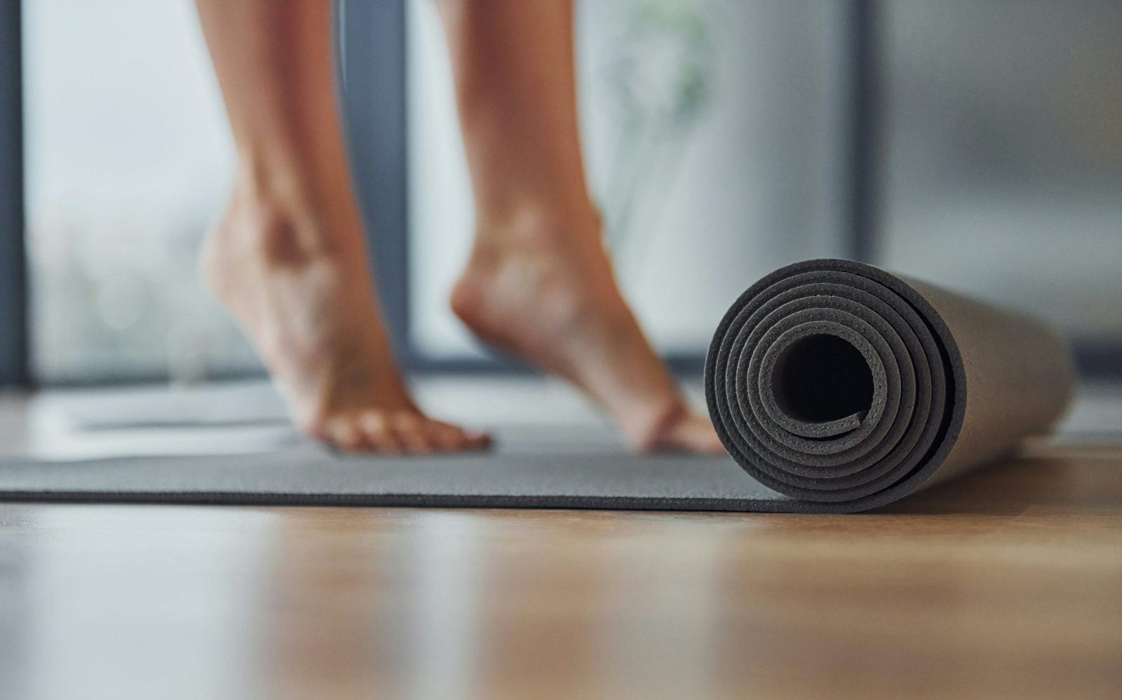 Bare feet on tiptoe beside a half-rolled yoga mat on a wood floor
