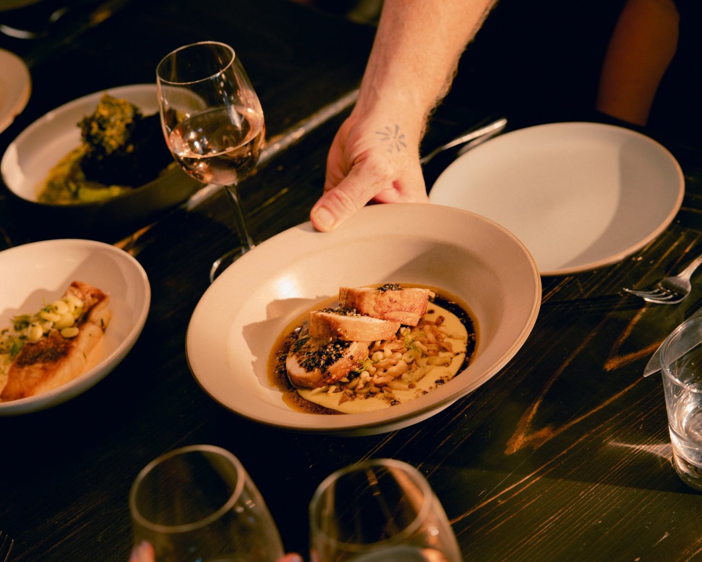 A plated dinner being set down beside glasses of wine