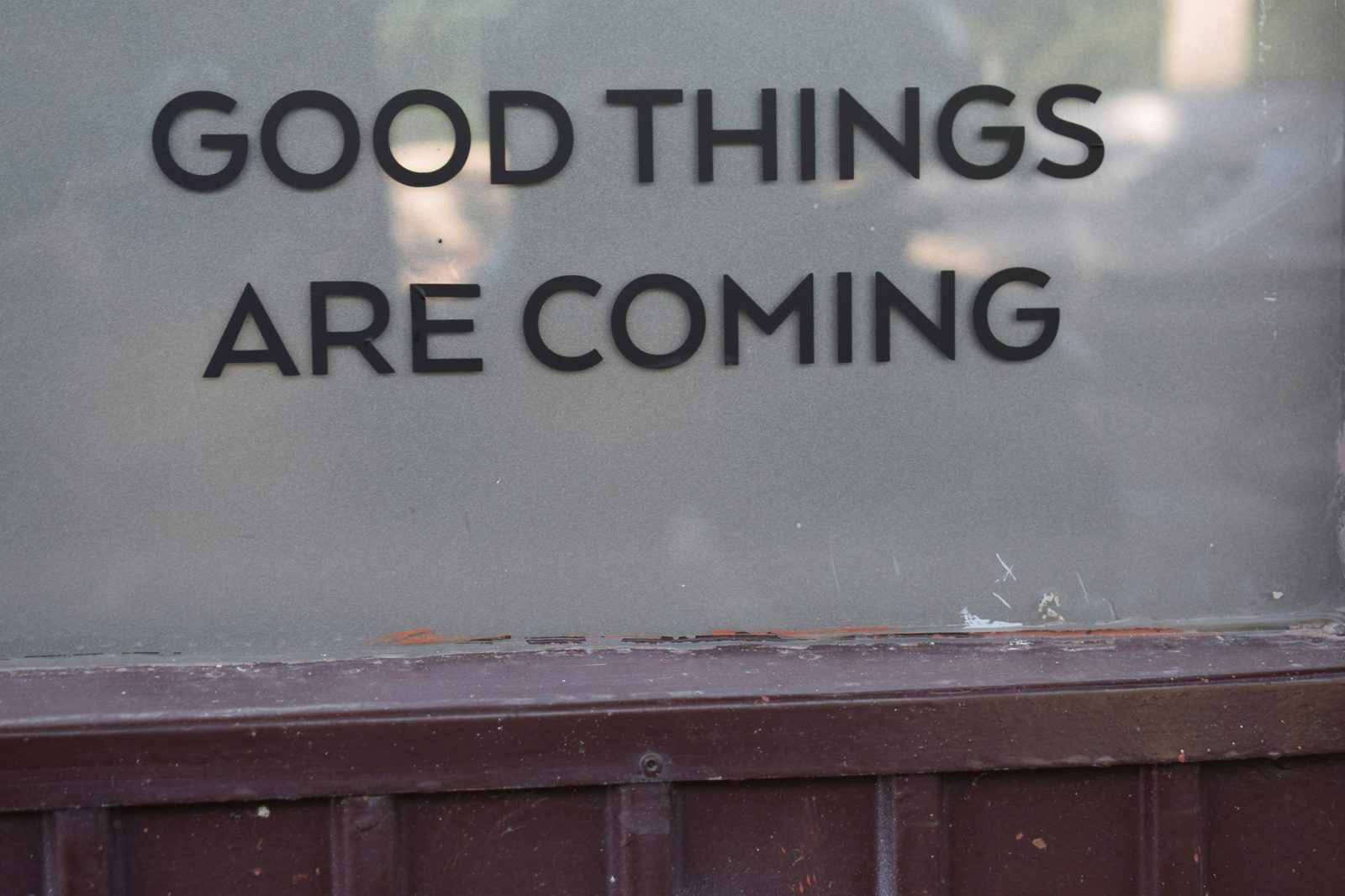 A shop window with GOOD THINGS ARE COMING in black letters above a dark painted sill